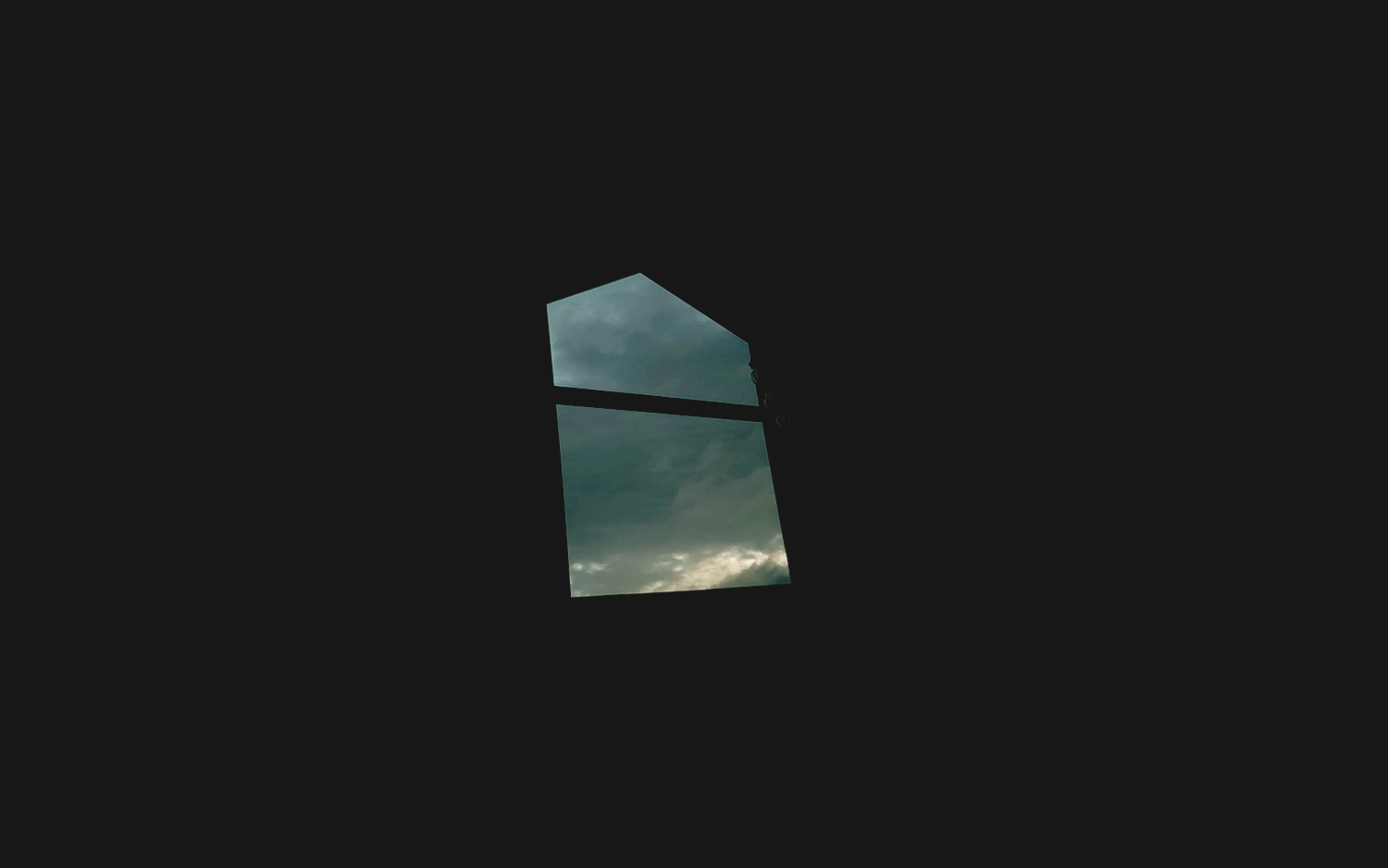 A small window framing cloudy sky inside a dark room