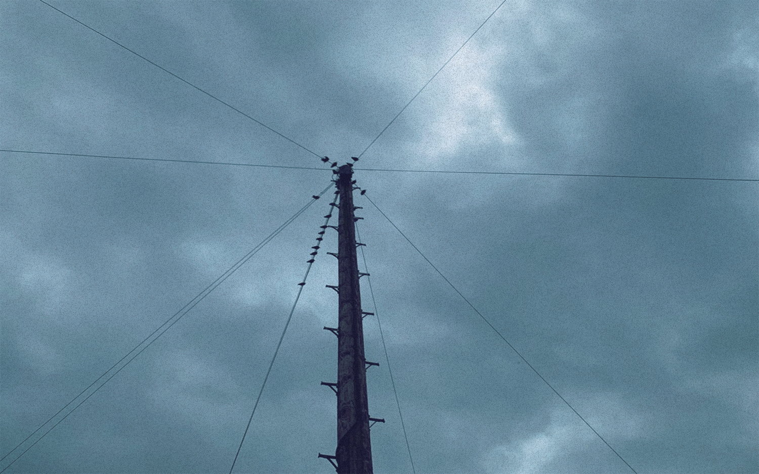 An overhead mast and wires against a cloudy blue sky